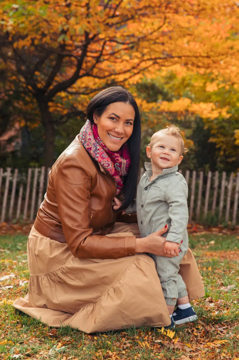 Playloop founder Nicole kneeling on autumn leaves in a park, smiling with her toddler son Giovanni