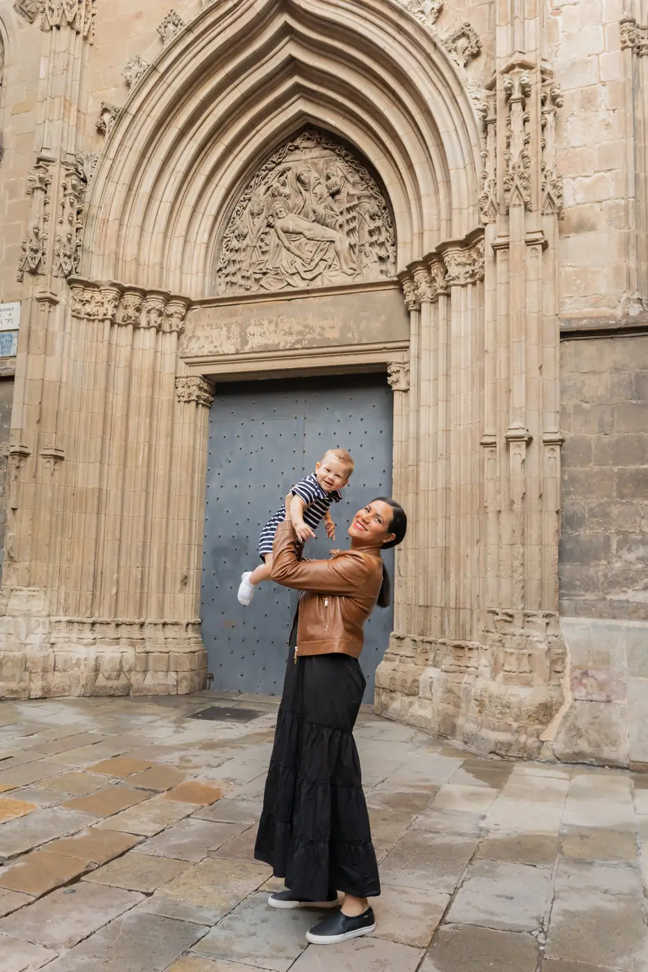 Nicole lifting baby Giovanni into the air outside a Gothic cathedral doorway in Barcelona