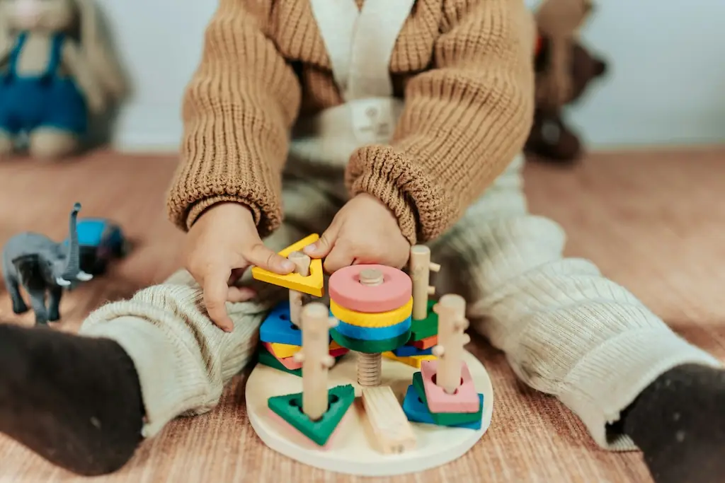 Child in a knitted cardigan fitting a yellow triangle onto a colourful wooden stacking-shapes toy