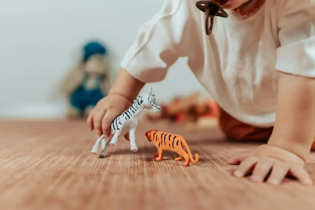 Child's hands walking a toy zebra towards a toy tiger across a woven rug